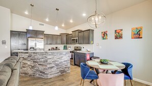 Une cuisine moderne dotée de plans de travail en granit, d’un îlot central intégré et d’un coin repas avec des chaises bleues et roses.