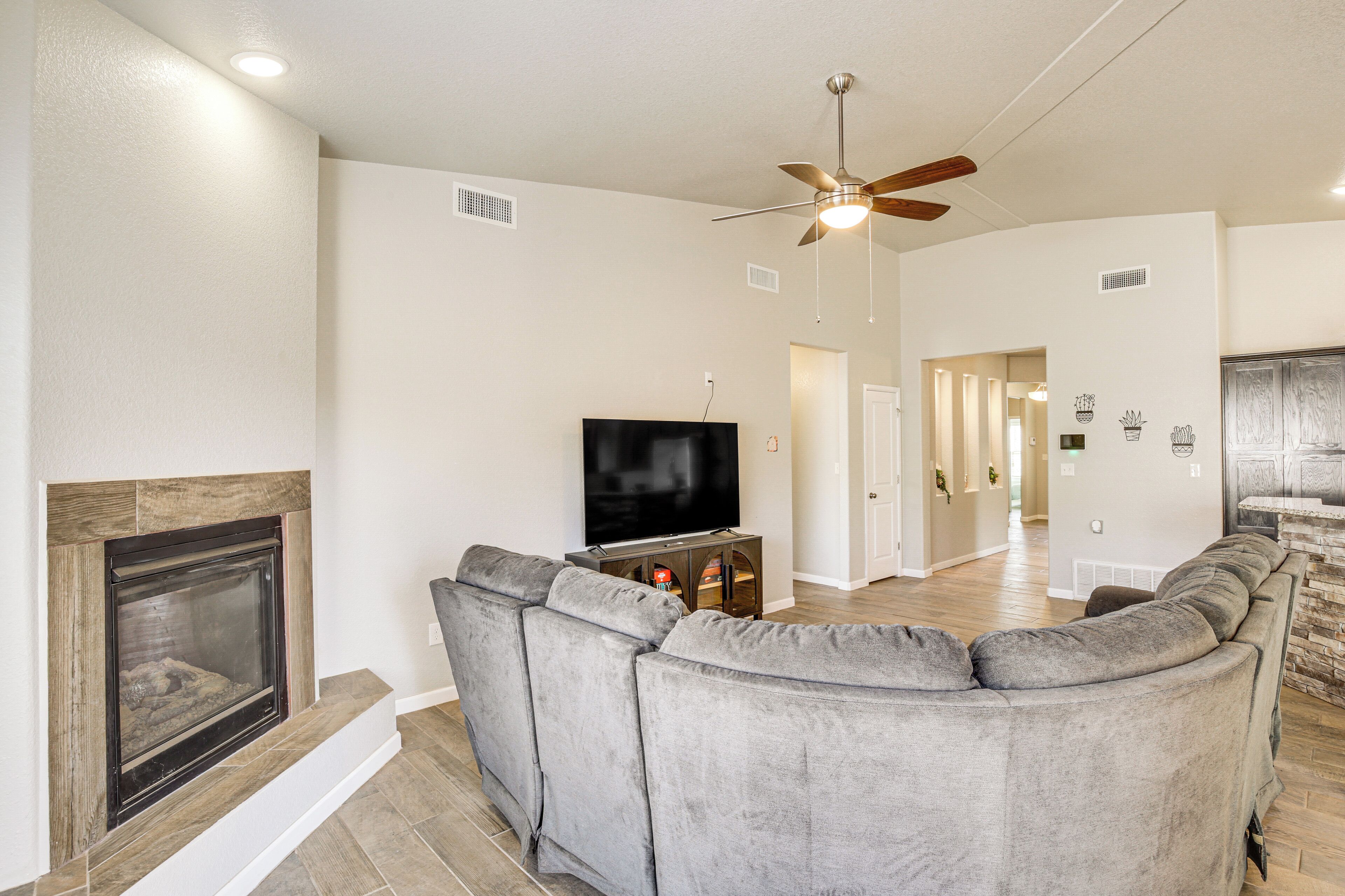 A modern living room with a fireplace, a large grey sectional sofa, a flat-screen TV, and a ceiling fan.
