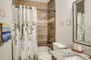 Une salle de bain avec un rideau de douche, des toilettes, un lavabo doté d’un plan de travail en marbre et un miroir.
