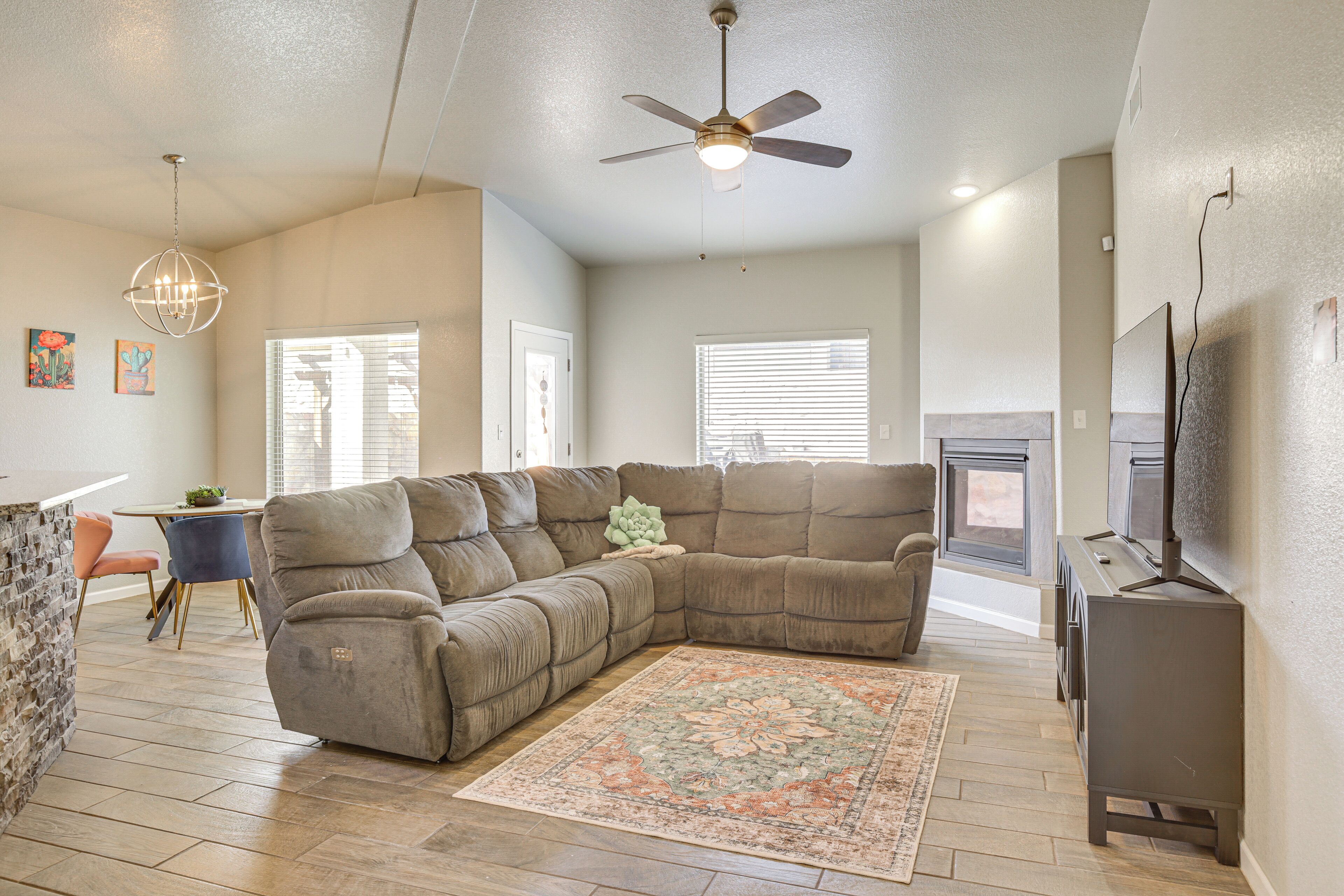 A living room with a sectional sofa, a ceiling fan, a fireplace, and a dining area with a table and chairs.