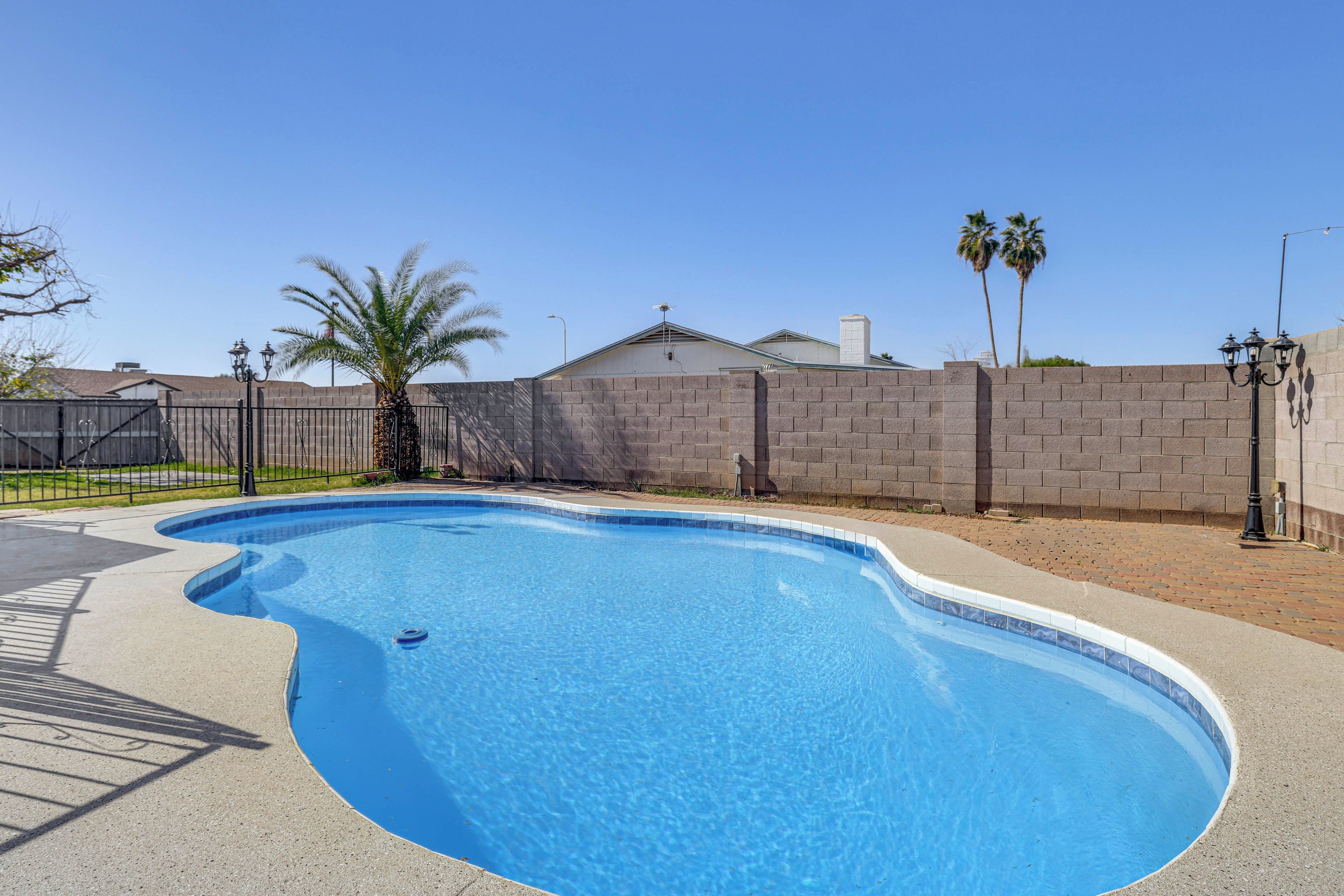 A swimming pool with a curved edge, surrounded by a brick wall and a fence.