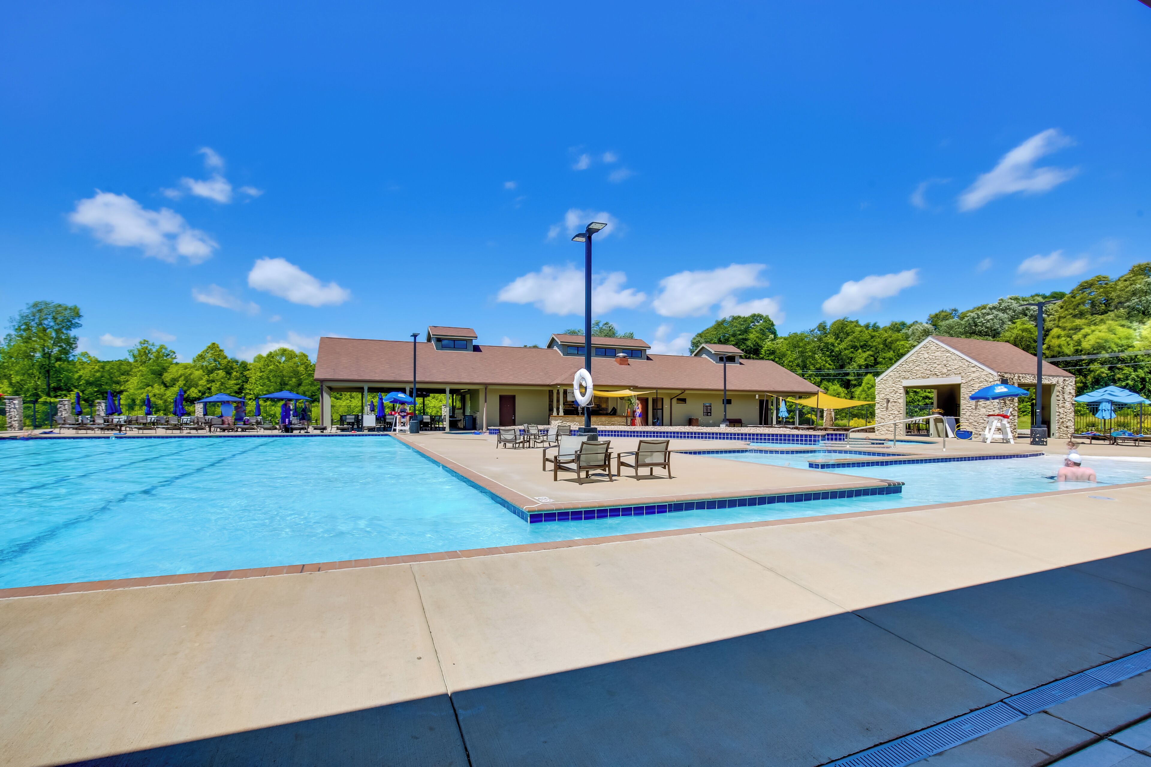 A swimming pool area with lounge chairs and umbrellas, a covered seating area, and a stone building.