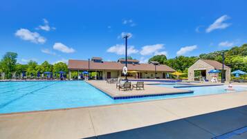A swimming pool area with lounge chairs and umbrellas, a covered seating area, and a stone building.