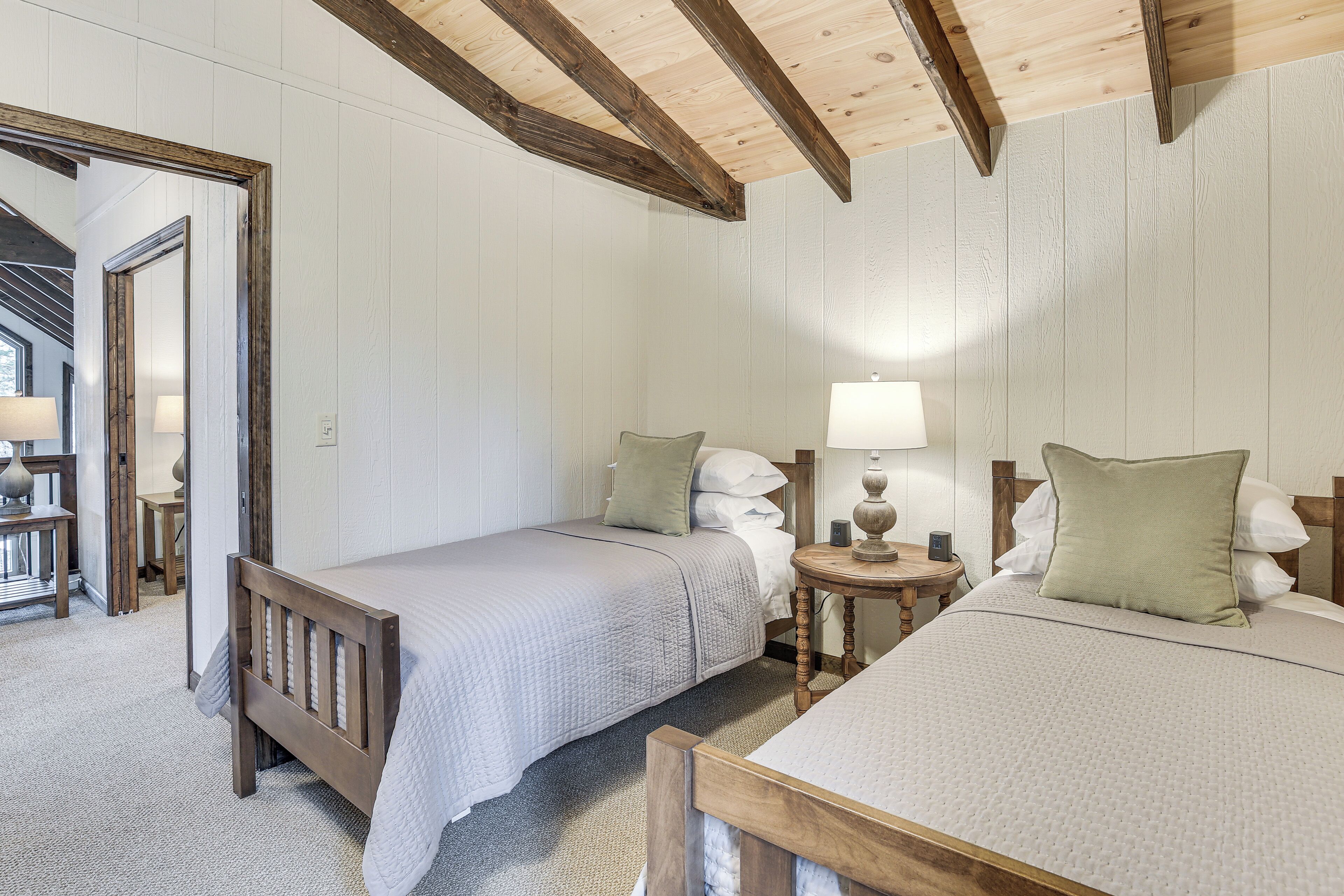 Una habitación con dos camas, vigas de madera en el techo y una pequeña mesa redonda con una lámpara.