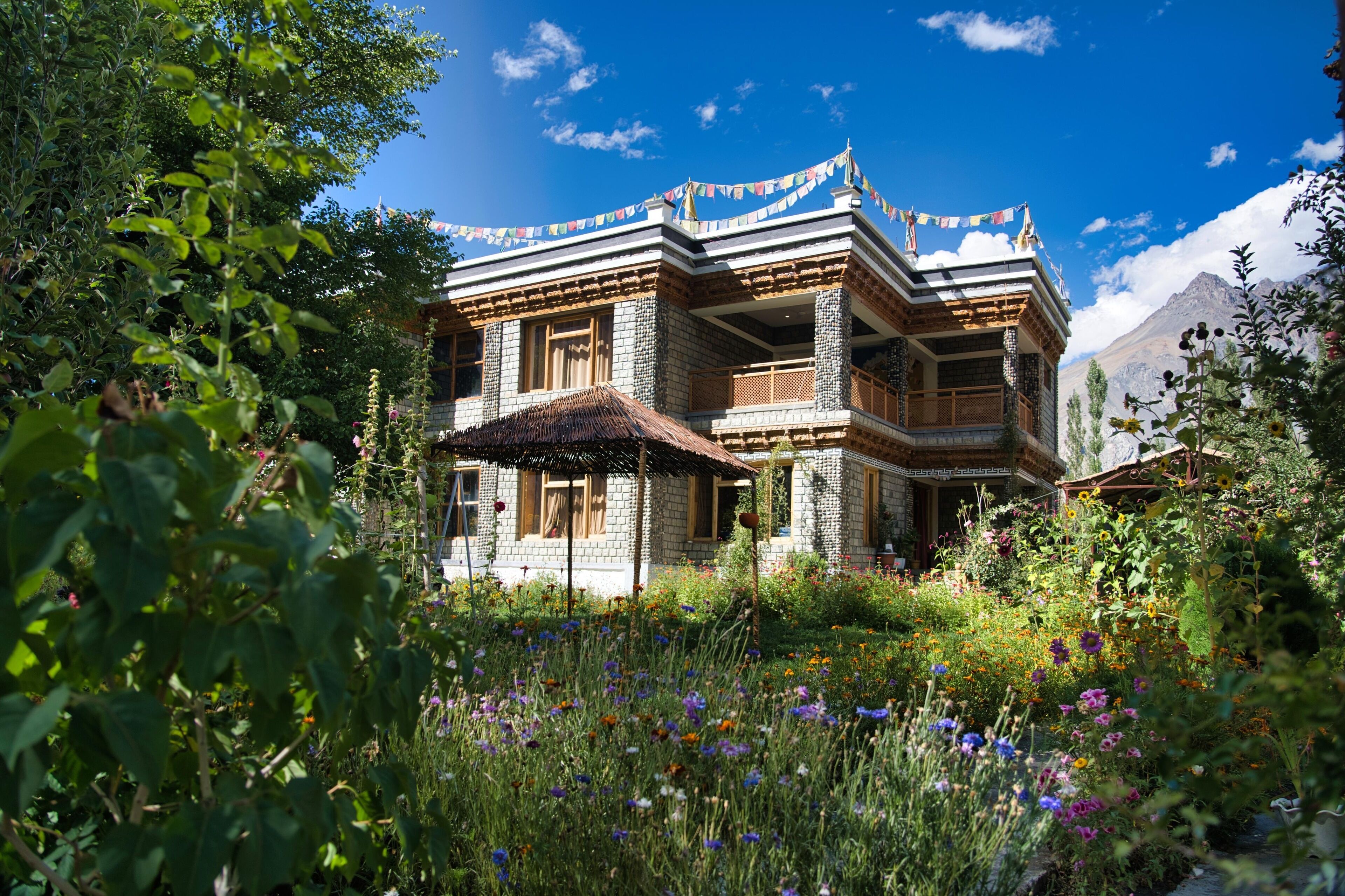A traditional multi-story building with a thatched-roof structure in front, surrounded by a vibrant garden with various wildflowers.