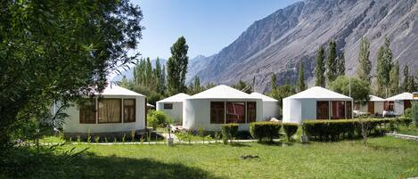 Yurts with a mountain backdrop, surrounded by greenery and a well-maintained lawn.