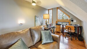 A cozy attic room with a leather sofa, a desk with a computer, and a window overlooking trees. - Family-friendly Perks! Secluded Tuckasegee Haven (Tuckasegee)