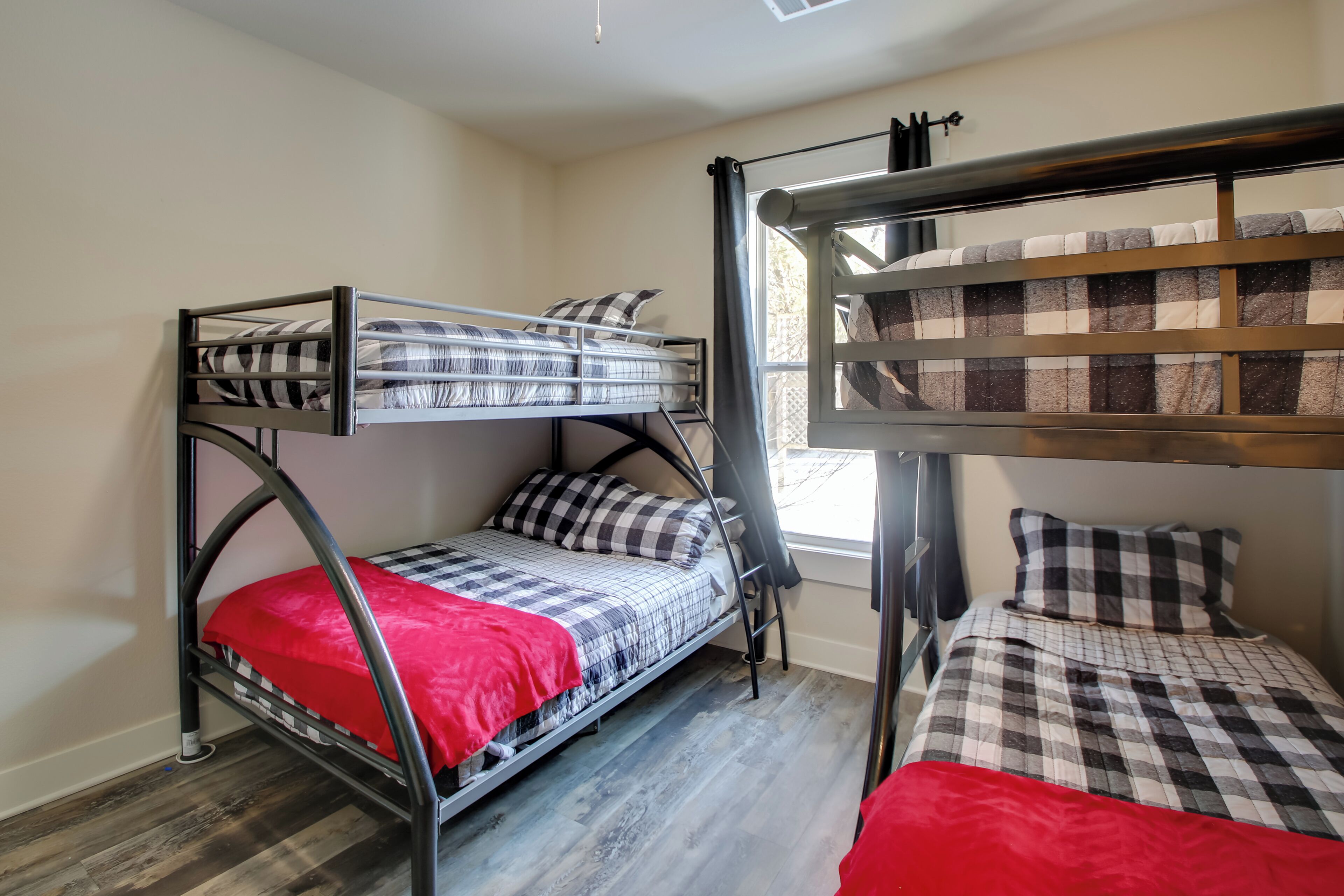 A dormitory room with two bunk beds, a window with curtains, and a red blanket on one bed.