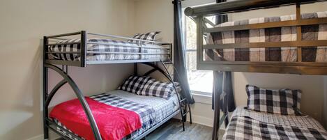 A dormitory room with two bunk beds, a window with curtains, and a red blanket on one bed.