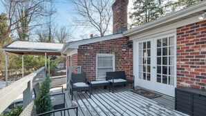 Une terrasse en bois avec des meubles d’extérieur, une maison en briques et un espace abrité.