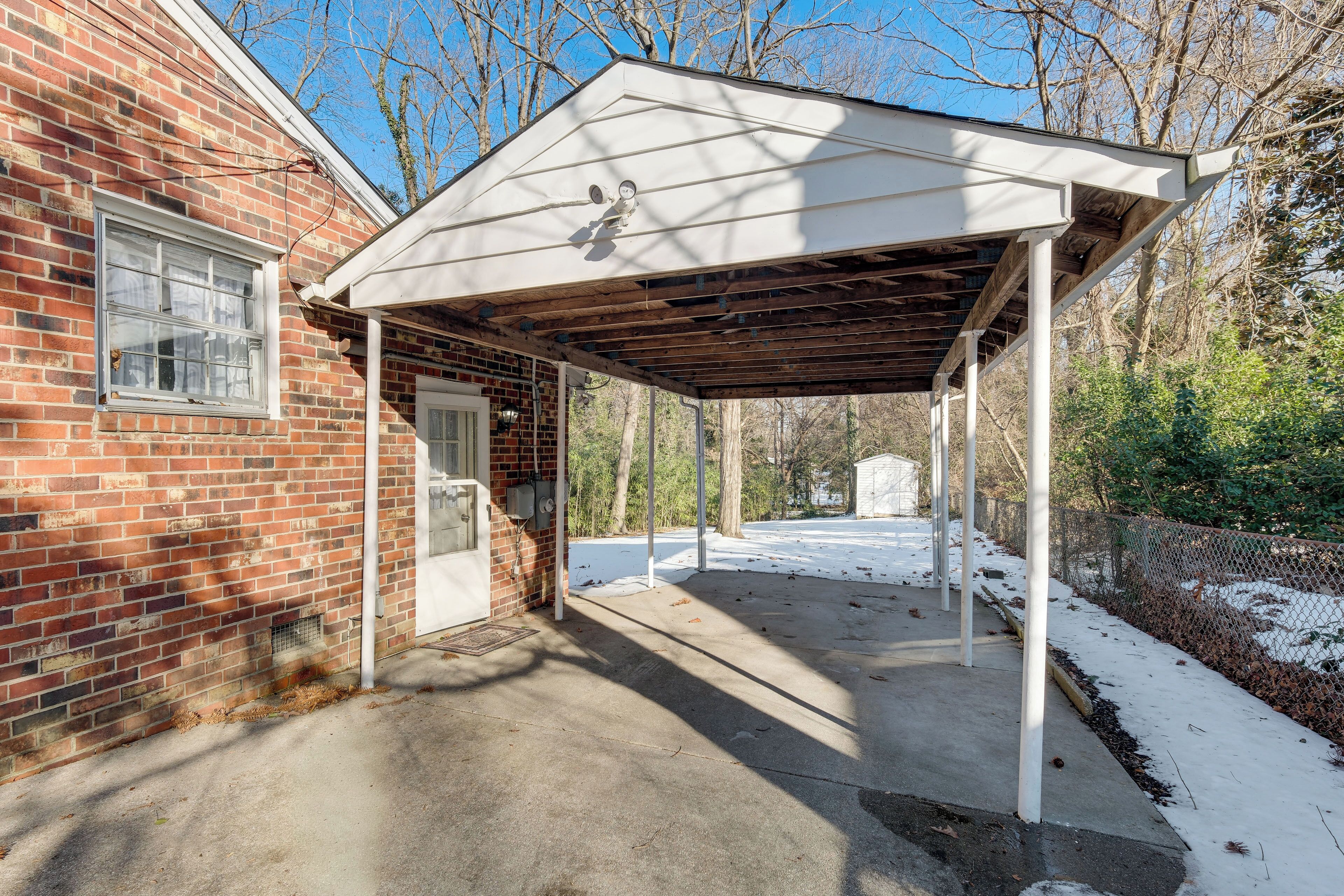 A covered patio area with a brick building, a door, and a concrete path.