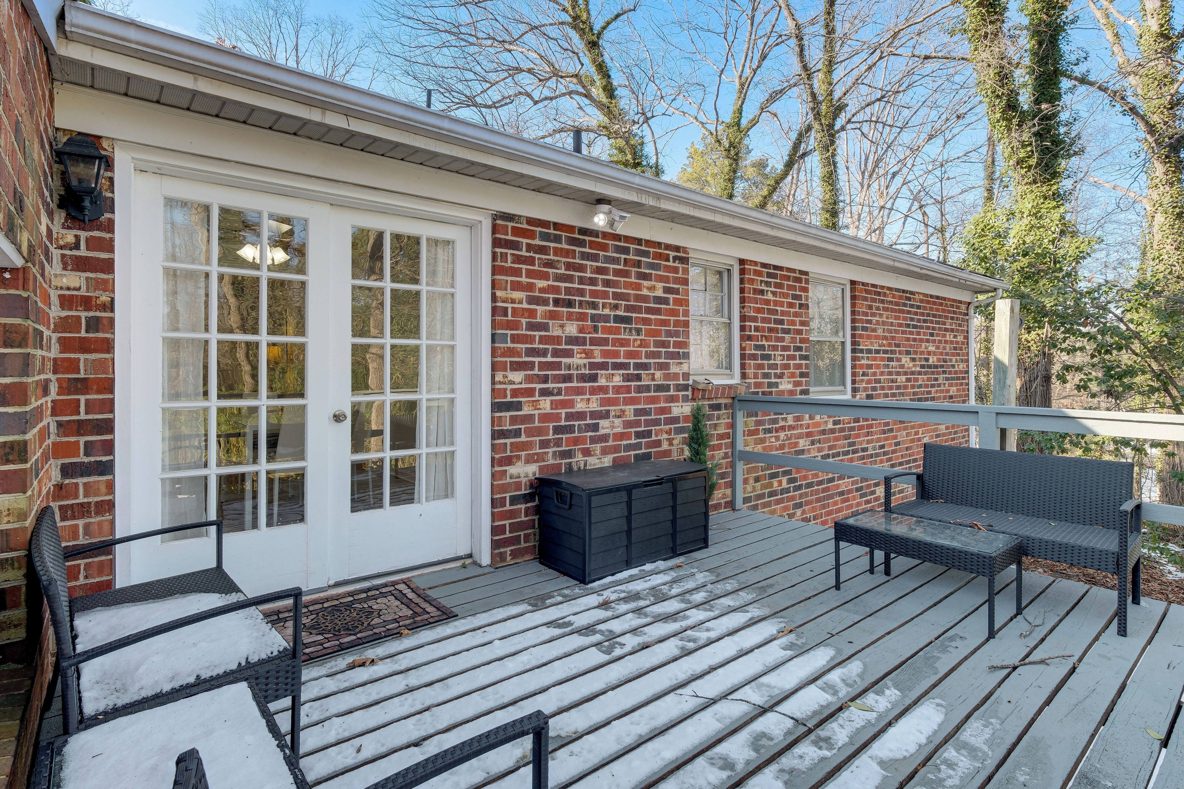 A covered deck with a brick house, a bench, and a small table.