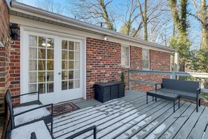 A covered deck with a brick house, a bench, and a small table.