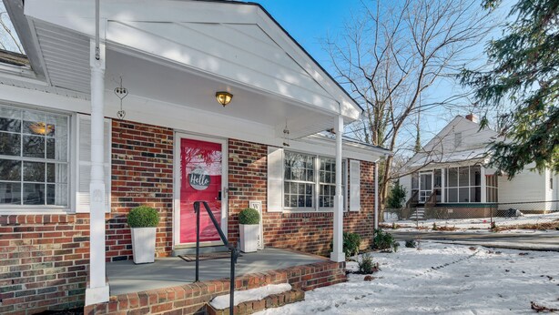 Une maison à deux étages avec une façade en briques, des éléments décoratifs blancs et une porte rouge.