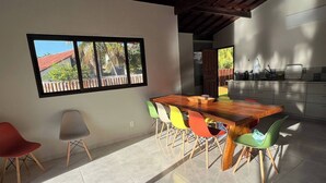 Een moderne keuken met een houten tafel en kleurrijke stoelen, een raam met uitzicht op een gebouw met rode daken, en een betegelde vloer.