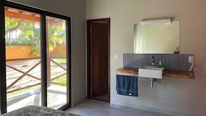 Een kamer met een schuifdeur naar buiten, een klein wastafeltje met spiegel, en een betegelde spatwand.
