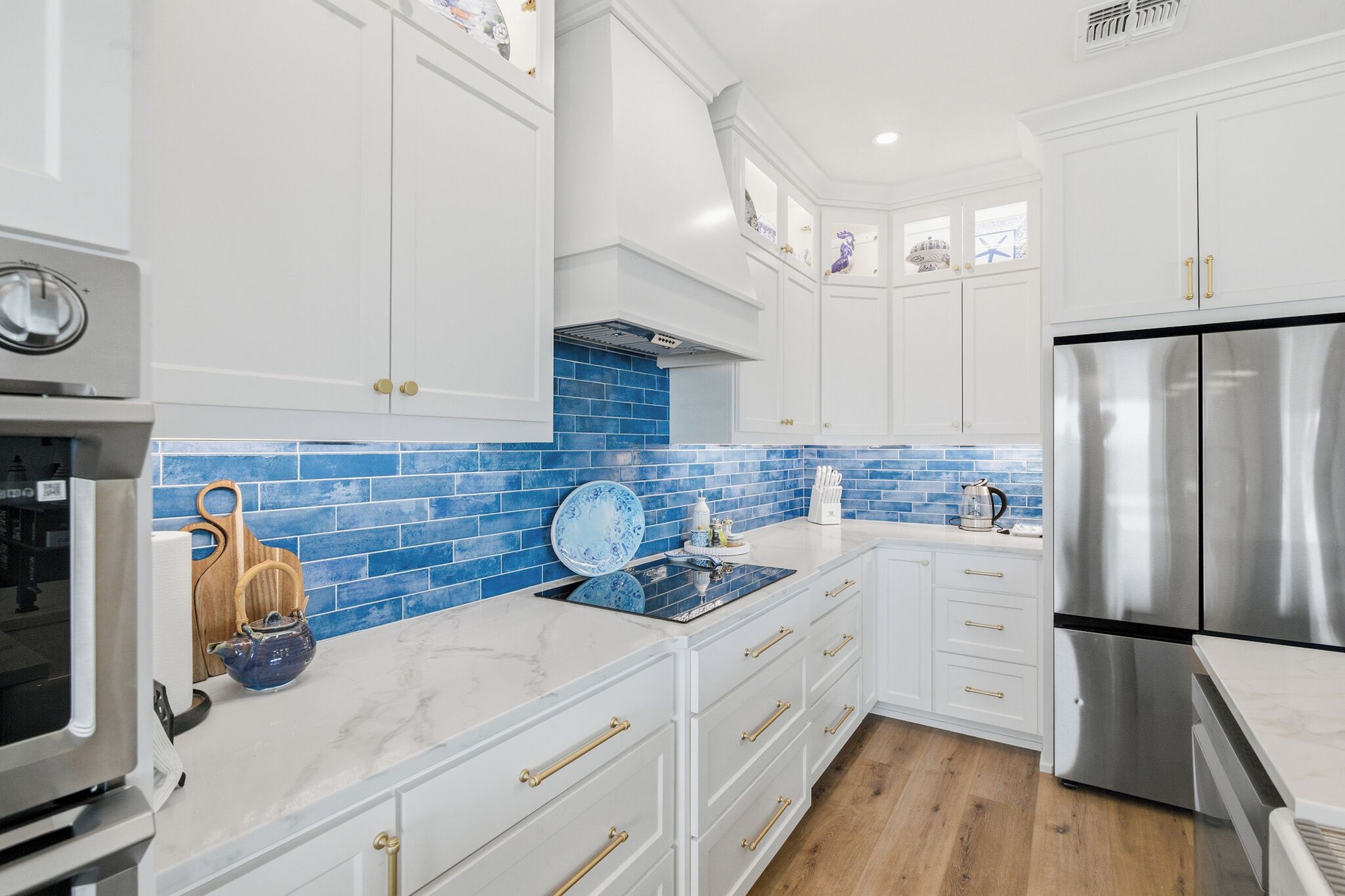 A modern kitchen with white cabinets, a blue-tiled backsplash, stainless steel appliances, and wooden utensils on the counter.