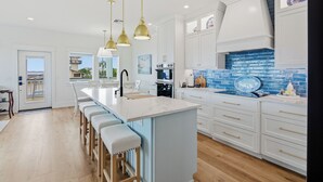 A modern kitchen with a central island, white cabinetry, and blue backsplash. - Coastal Breeze Cottage near beach water views (Port O'Connor)