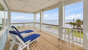 A covered outdoor area with wooden flooring, white railings, and two blue cushioned lounge chairs. - Coastal Breeze Cottage near beach water views (Port O'Connor)