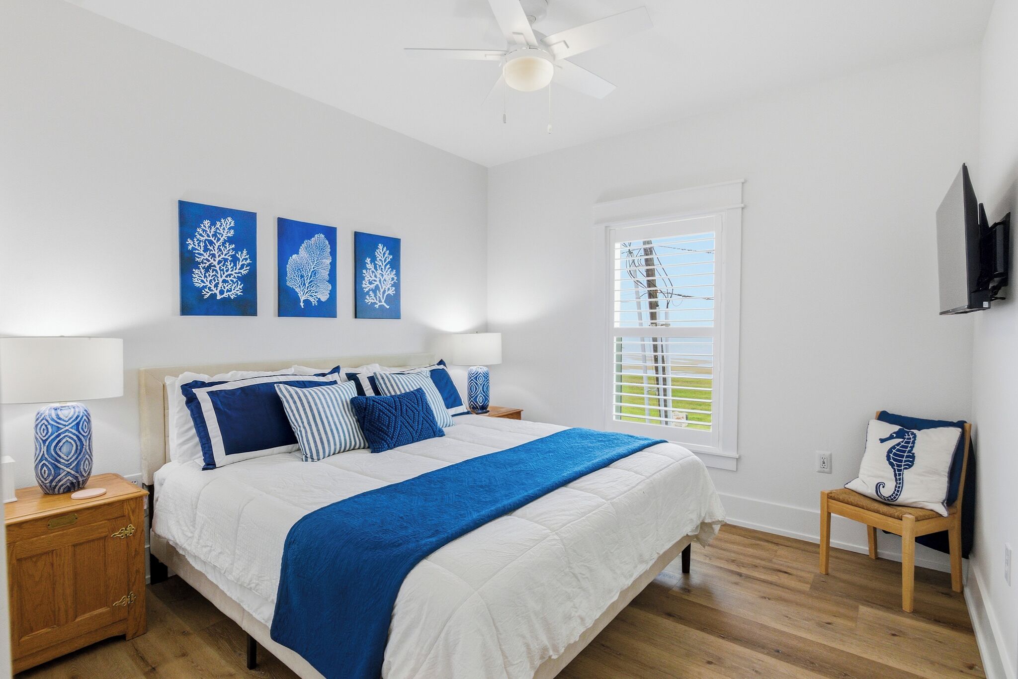 A bedroom with a bed, a nightstand, a chair, a window, and artwork on the wall.