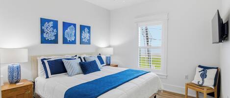 A bedroom with a bed, a nightstand, a chair, a window, and artwork on the wall.