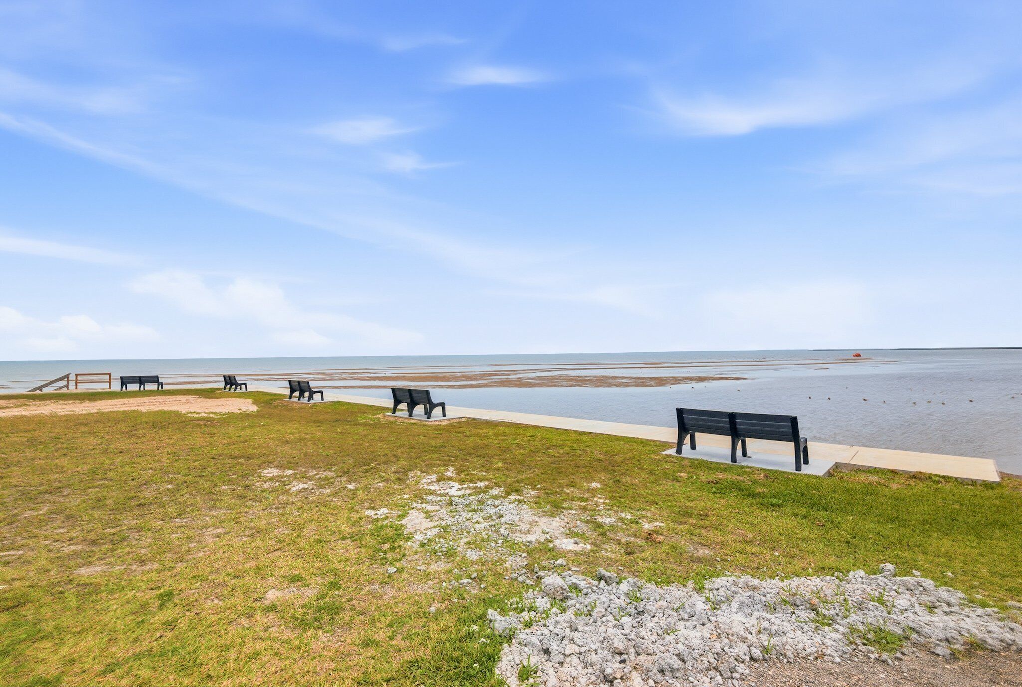 A grassy area with benches and a pathway leading to a beach.