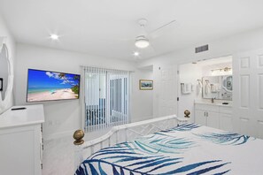 Un dormitorio con cama, televisor, balcón con vista a la playa y baño con espejo y lavamanos.
