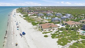 Vista aérea de un complejo turístico costero con propiedades frente a la playa, una playa de arena y una vista despejada del océano.