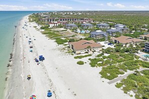 Vue aérienne d’une station balnéaire avec des propriétés situées en bord de mer, une plage de sable et une vue dégagée sur l’océan.