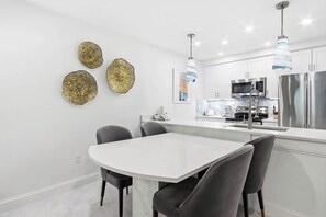 Una cocina moderna con armarios blancos, electrodomésticos de acero inoxidable y una mesa de comedor blanca con cuatro sillas.