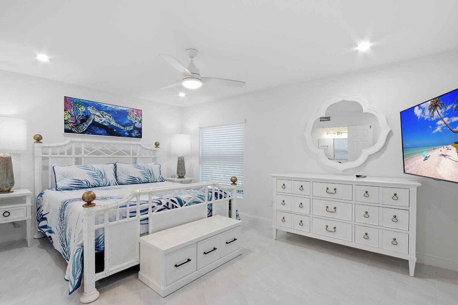 Un dormitorio con cama blanca, mesita de noche, cómoda y ventilador de techo, además de un cuadro.