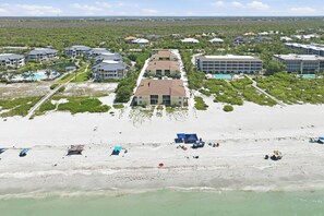 Un hotel frente al mar con varias construcciones, una playa con sombrillas y una vista despejada del océano.