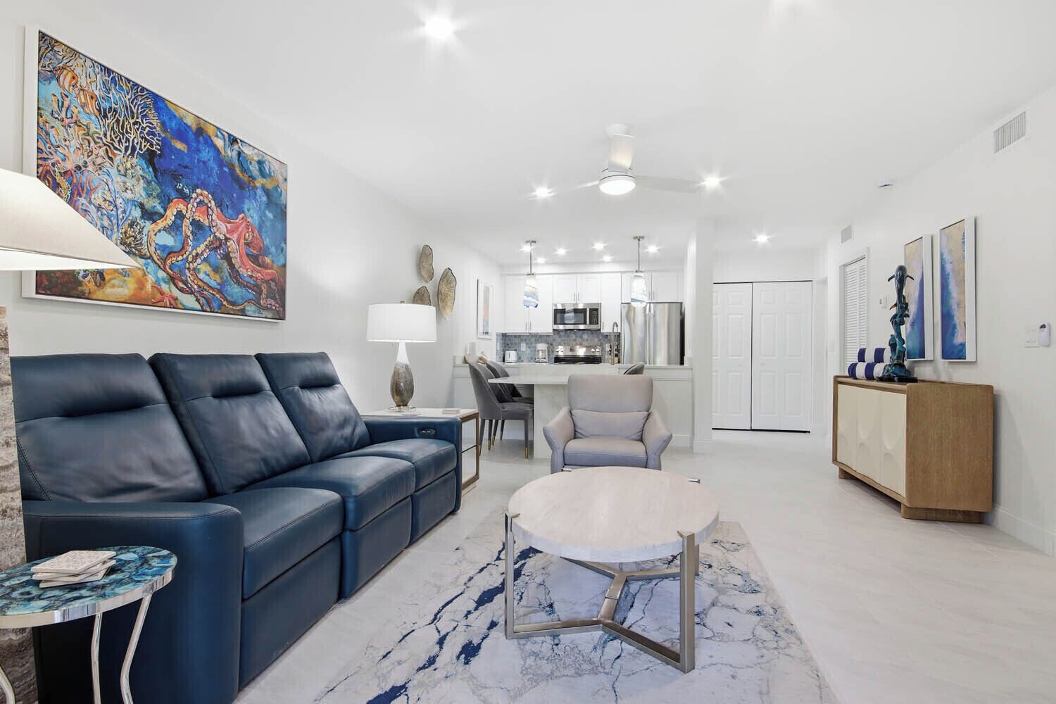A modern living room with a blue sofa, a round coffee table, and a dining area in the background.