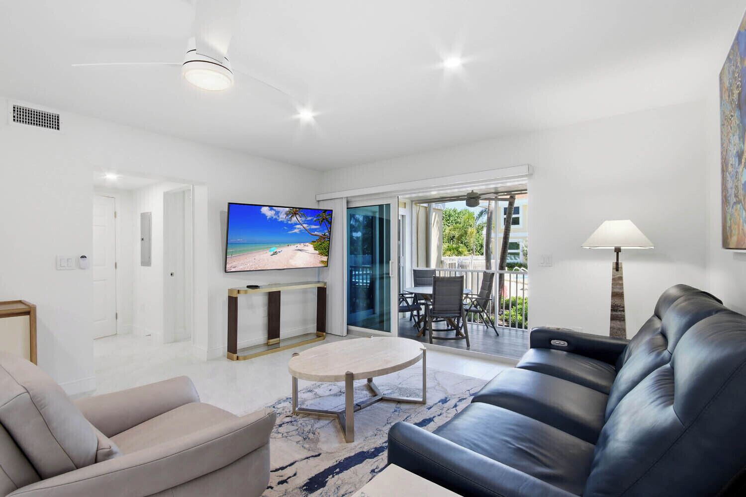 A modern living room with a flat-screen TV, a sofa, a coffee table, and a balcony with outdoor furniture.