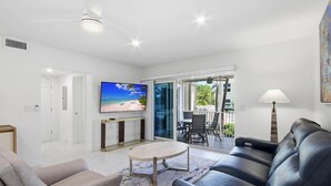 Una sala de estar moderna con una televisión de pantalla plana, un sofá, una mesa de centro y un balcón con mobiliario exterior.