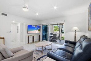 Un salon moderne doté d’un téléviseur à écran plat, d’un canapé, d’une table basse et d’un balcon aménagé avec du mobilier d’extérieur.