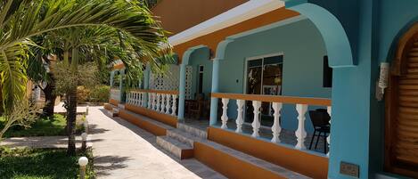 A building with a covered walkway, palm trees, and a staircase leading to a porch.