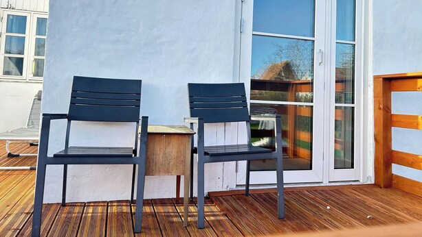 Une terrasse avec deux chaises et une petite table, une porte-fenêtre coulissante et une terrasse en bois.