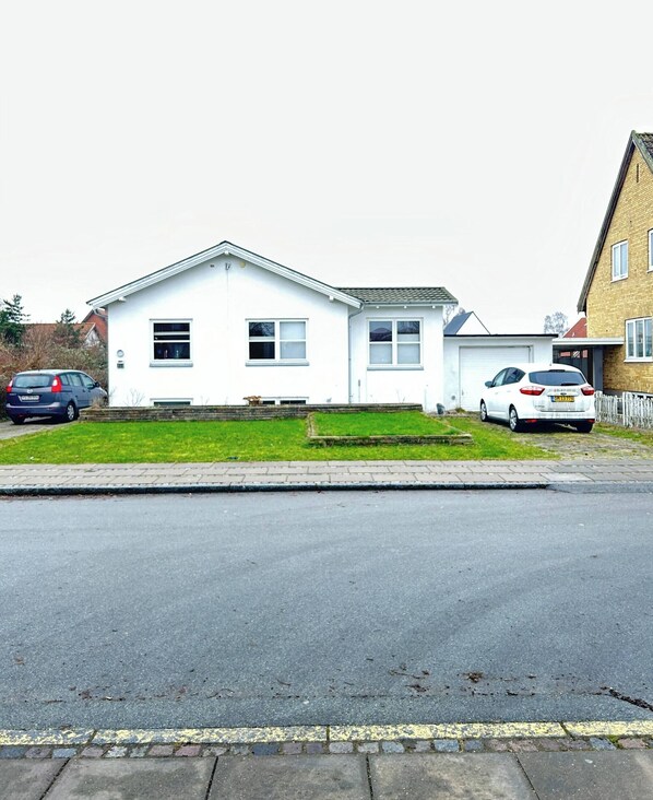 A two-story house with a front lawn, a driveway, and two parked cars. - Basement Apartment in Villa (Odense)