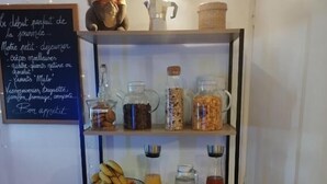 A breakfast bar with a variety of food items and beverages, including a basket of fruits, a pitcher of orange juice, and a selection of condiments.