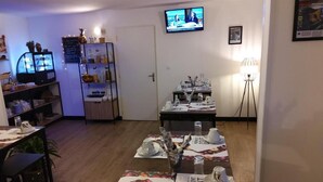 A dining area with a long table set for a meal, a television mounted on the wall, and a shelf with various items.