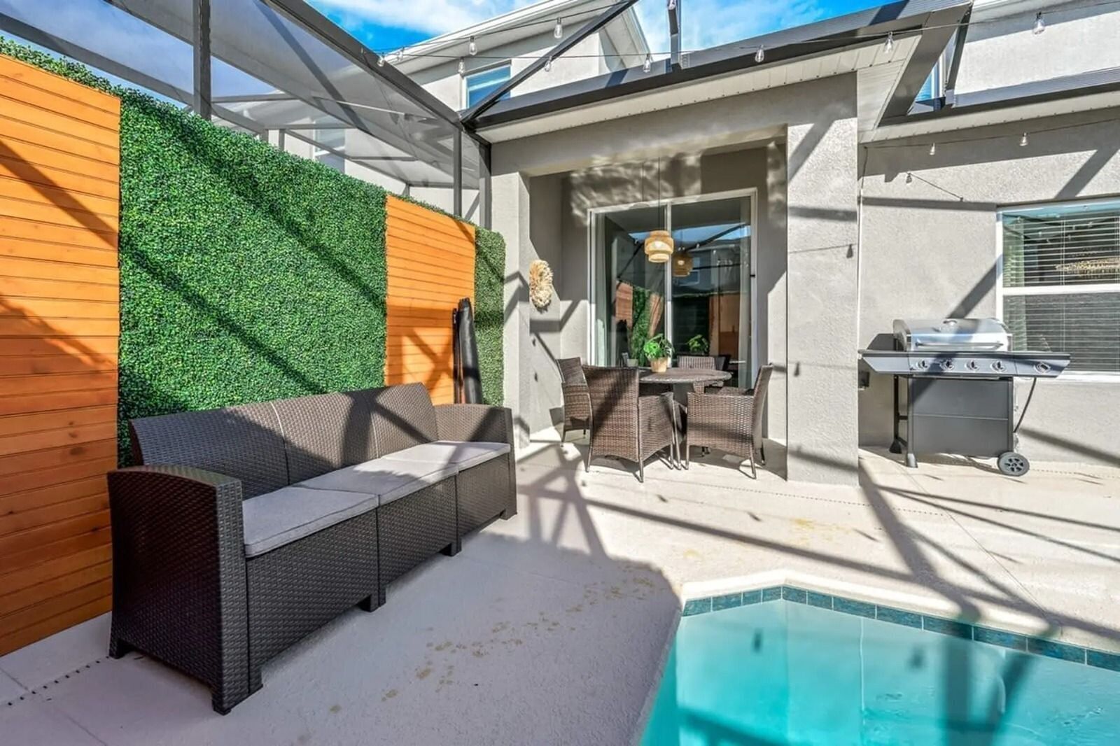 A modern outdoor patio with a pool, a dining area, and a barbecue setup.