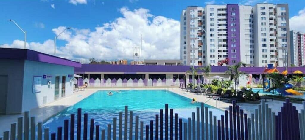 A swimming pool with a fence, a covered area, and tall buildings in the background.