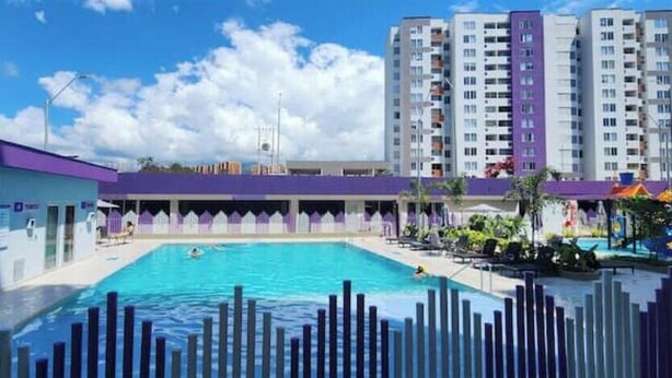 Una piscina con recinzione, zona coperta e alti edifici sullo sfondo.