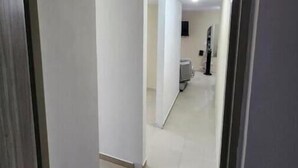 Un corridoio con pareti bianche e pavimento piastrellato che conduce a una stanza con un letto e una finestra.