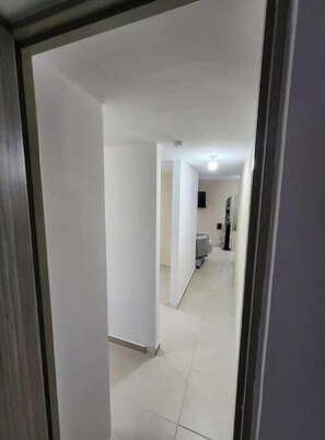 A hallway with white walls and a tiled floor leading to a room with a bed and a window. - 🌿 Rest on the Axis: Comfort, View and Privileged Location (Pereira)