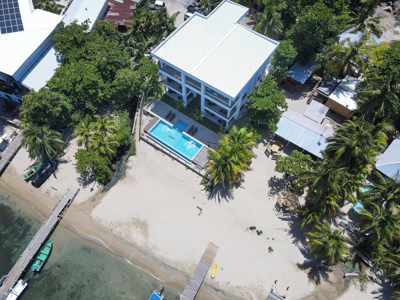 Vue aérienne d’une propriété située en bord de mer, avec une piscine, des palmiers et un quai.