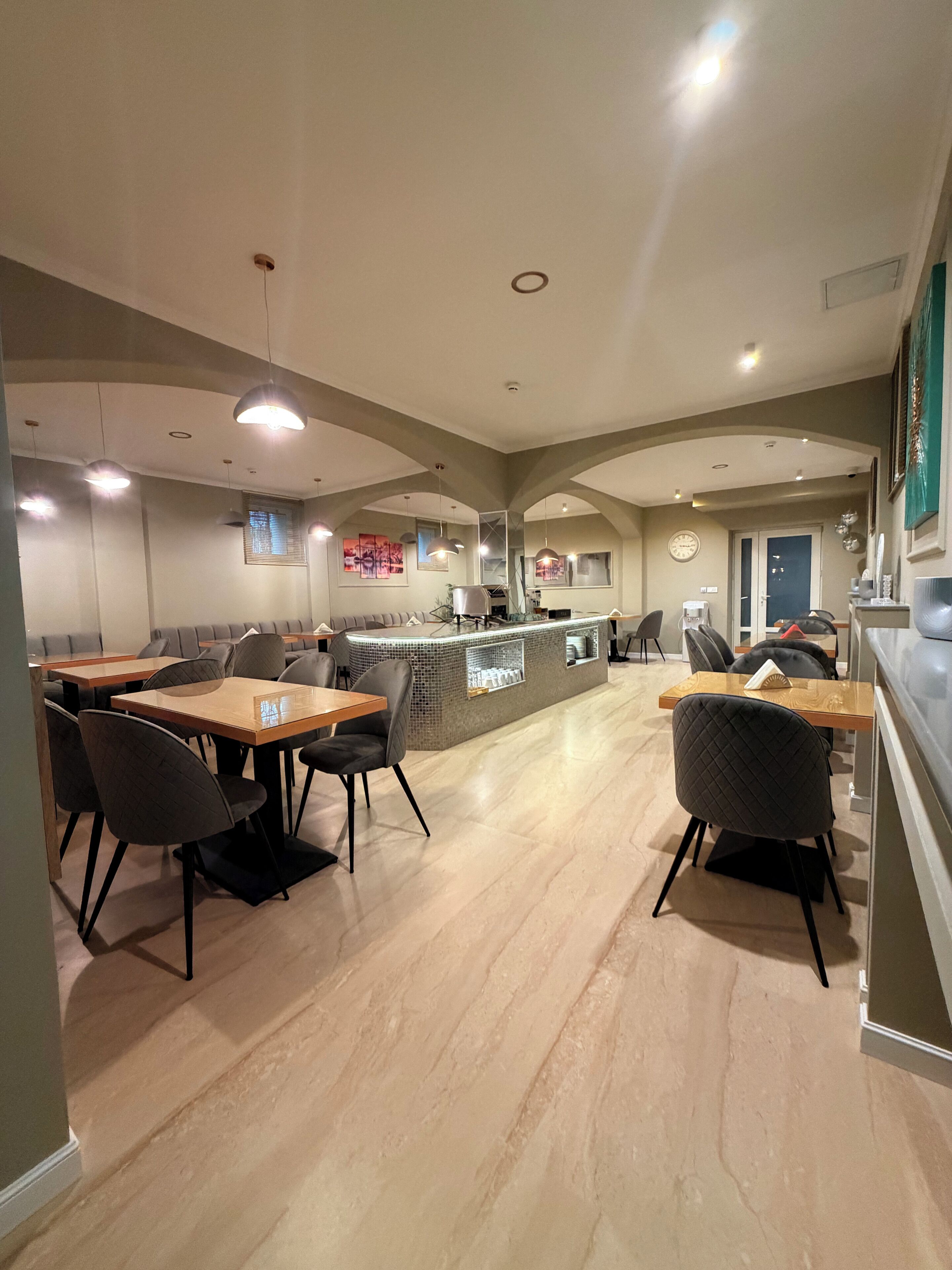 A modern restaurant with a central bar, seating areas, and a clock on the wall.