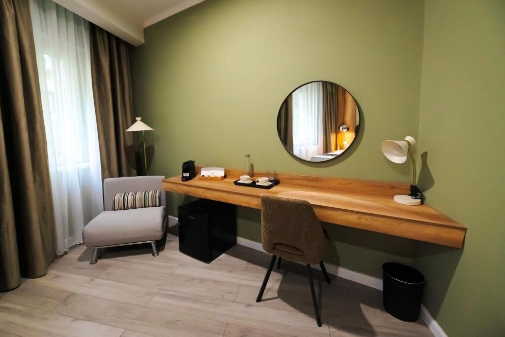 Una habitación con un escritorio de madera, una silla, un espejo, una lámpara y un cubo de basura.