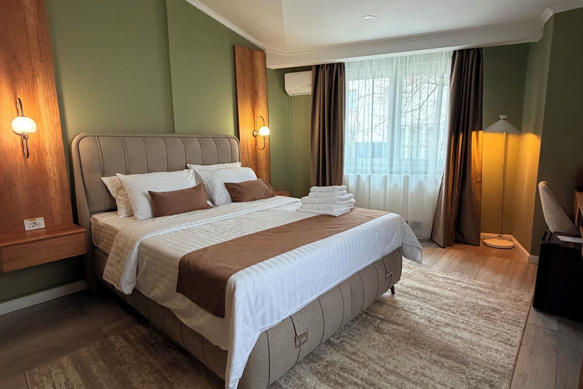 Un dormitorio con una cama grande, una mesita de noche, una lámpara y una ventana con cortinas.